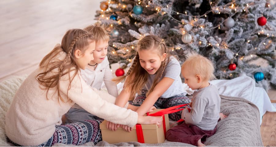 Siblings opening a present in the living room beside a Christmas tree.